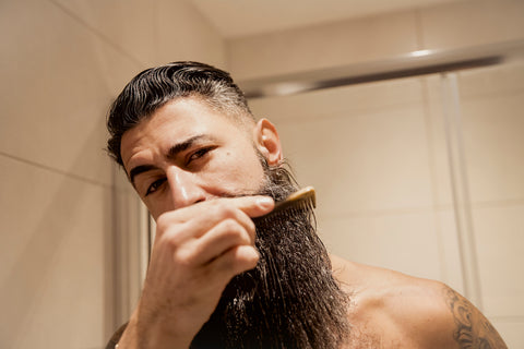 handsome guy combing beard oil through his long beard after a shower