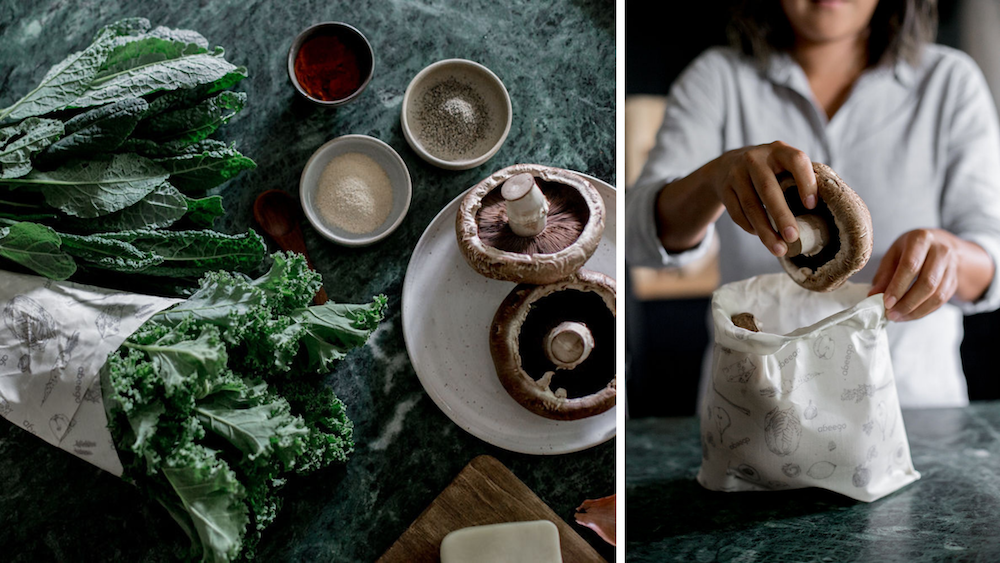 Kale wrapped in Abeego on the counter next to small spice dishes and a plate with portobello mushrooms. A Giant Abeego folded into a bag with hands putting portobello mushrooms inside. 