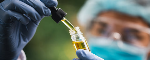 A bottle of synthetic nicotine being evaluated by a person wearing goggles, a hair net, a mask and gloves. 