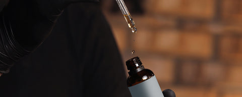 A drop of synthetic nicotine falling into a brown glass vape juice bottle. 