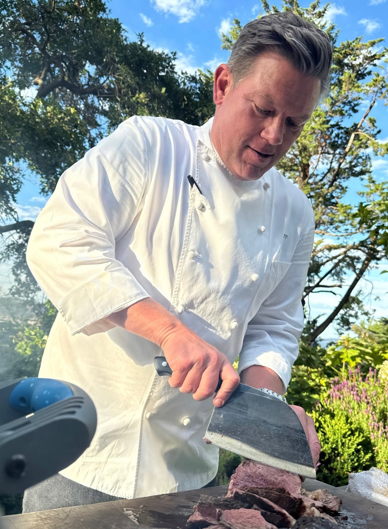 Chef in white uniform slicing meat outdoors.