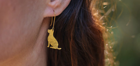 Images shows a close up of a brass dog earring, created exclusively for Guide Dogs by Just Trade and the Flowering Desert Project.