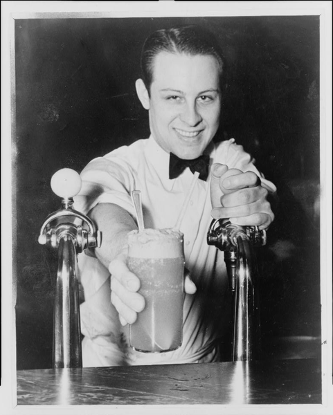 Soda Jerk handing over ice cream soda between two soda fountains