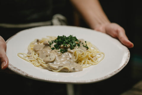 A person serving a mushroom pasta dish