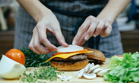 A person adding toppings to a portobello mushroom cap burger
