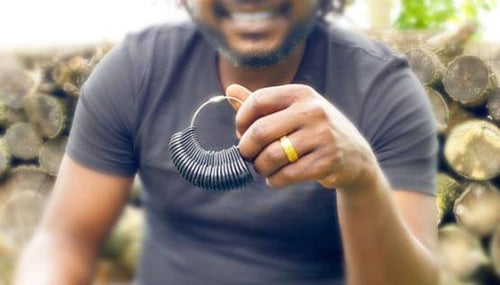 Man wearing gold wedding band holding up ring sizer tool. 