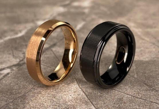 gold tungsten men's engagement ring and black tungsten engagement ring on tile background 