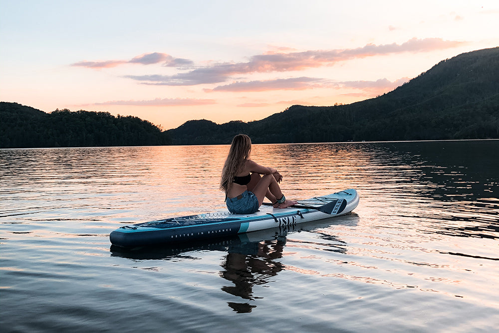 woman sitting on paddle board looking at sunset