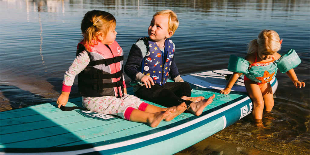 three young kids on a paddle board
