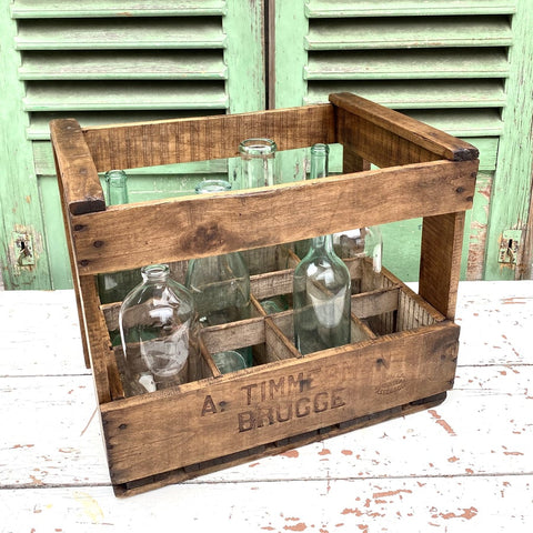 Vintage wooden brewery crate with a few empty glass bottles on a white wooden table with green shutters in background