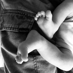 two small baby feet resting on a father's leg in black and white