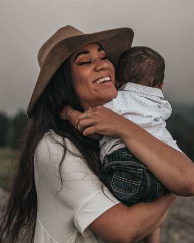 Mother hugging baby on Mother's Day smiling and wearing a large sun hat