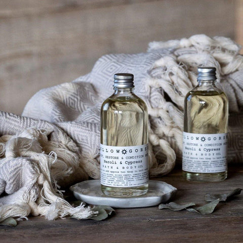 De-stress natural bath and body oil in two glass jars on a wooden table with beige cotton blankets behind