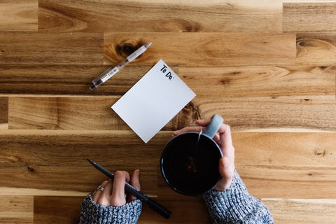 Woman holding mug of coffee in eco shop in Henley and writing to-do list on wooden table