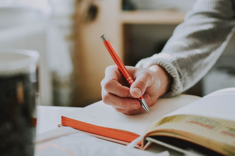 Member of our sustainable gift shop team in Henley writing in a notebook with an orange pen