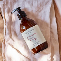 Geranium & Orange hand and body wash in sustainable glass bottle on cotton fabric