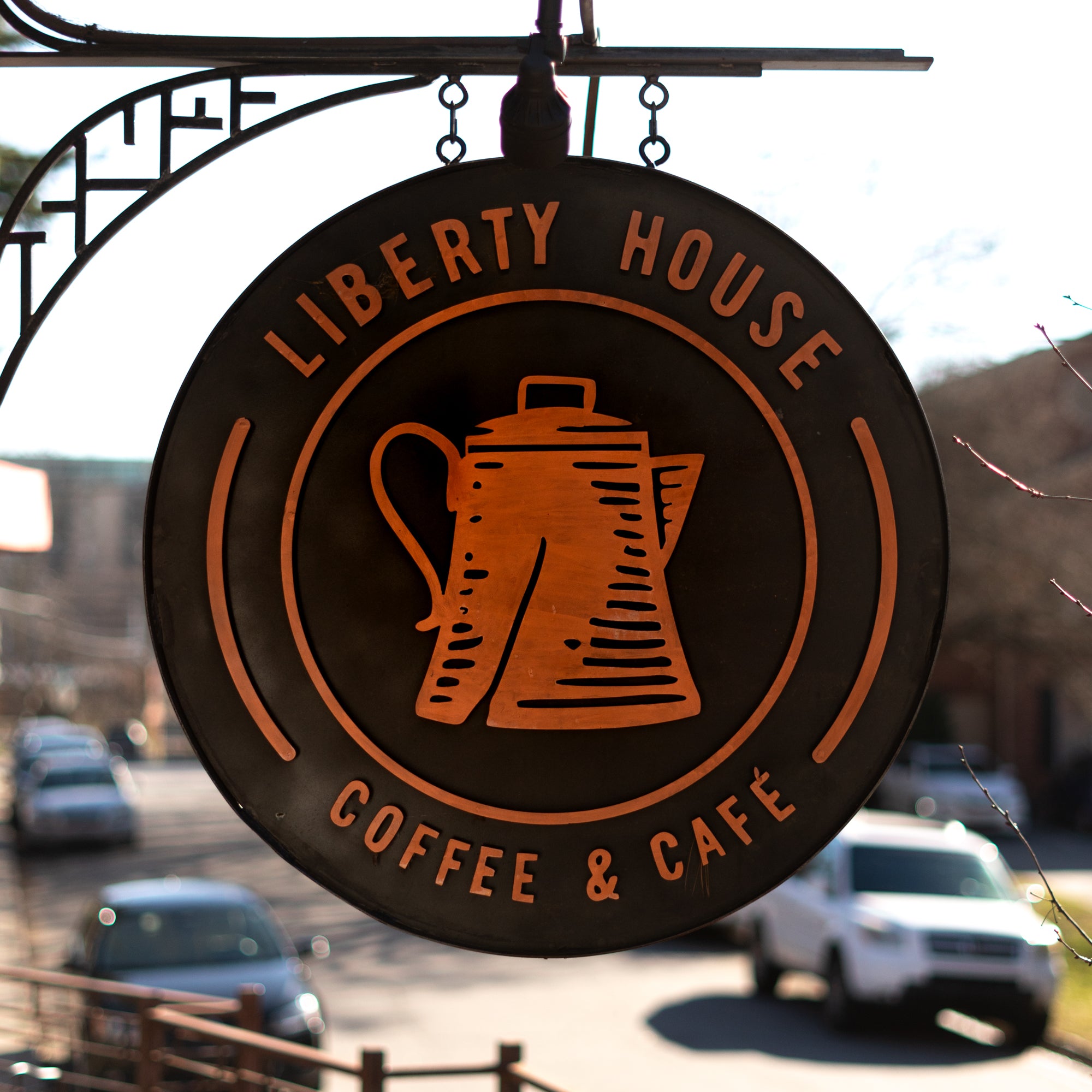 A black oval sign with Liberty House Coffee & Caffe written in orange, with a tea kettle in the middle of the sign.