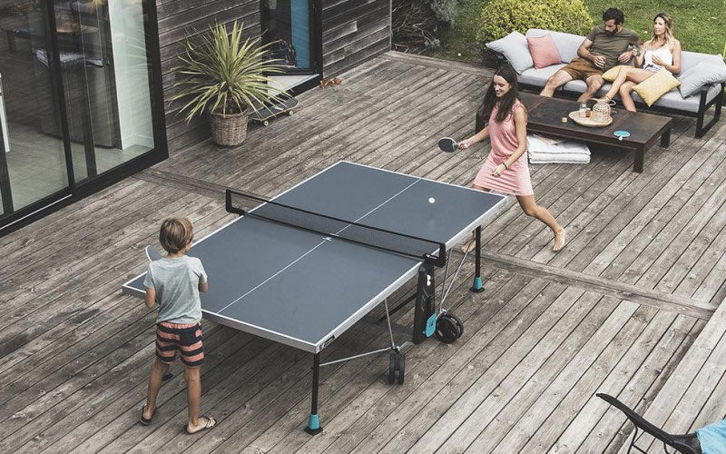 Two kids playing a game of table tennis with two adults sitting and watching