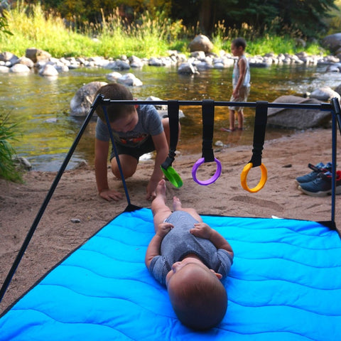 Baby on Lay and Play Adventure Mat, two older brothers in the background playing in river