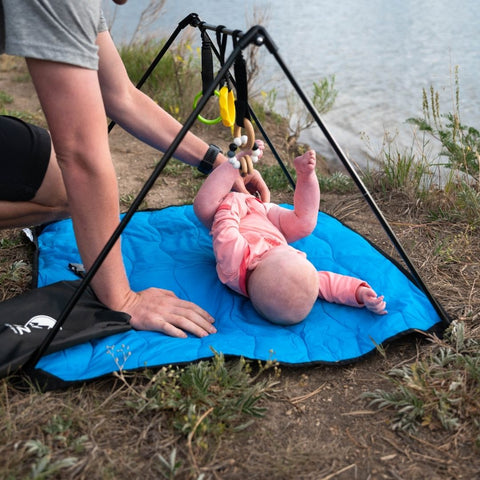 Baby on the Lay and Play Adventure Mat, dad's hands playing with baby, lake in background