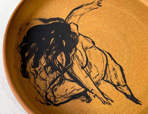 Image of a clay ceramic plate with a painting of a dancing nude woman with dark black hair flowing