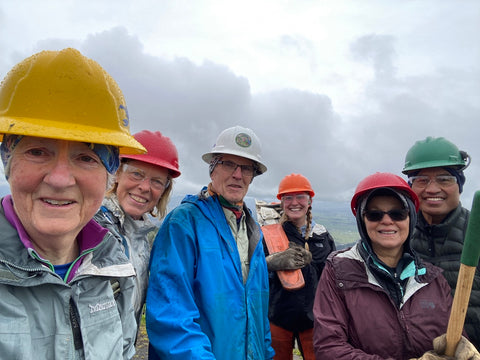 A group of volunteers smiling with hard hats on with a cloudscape behind them