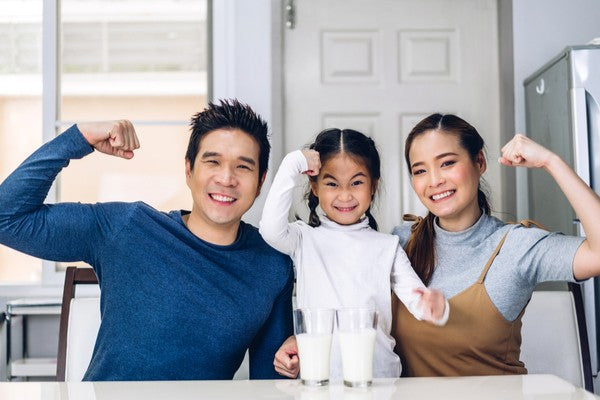 Portrait of enjoy happy love asian family father and mother with little asian girl smiling look at camara and having breakfast drinking and hold glasses of milk at table in kitchen