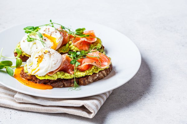 Toast with salmon, poached egg and avocado on a white plate.