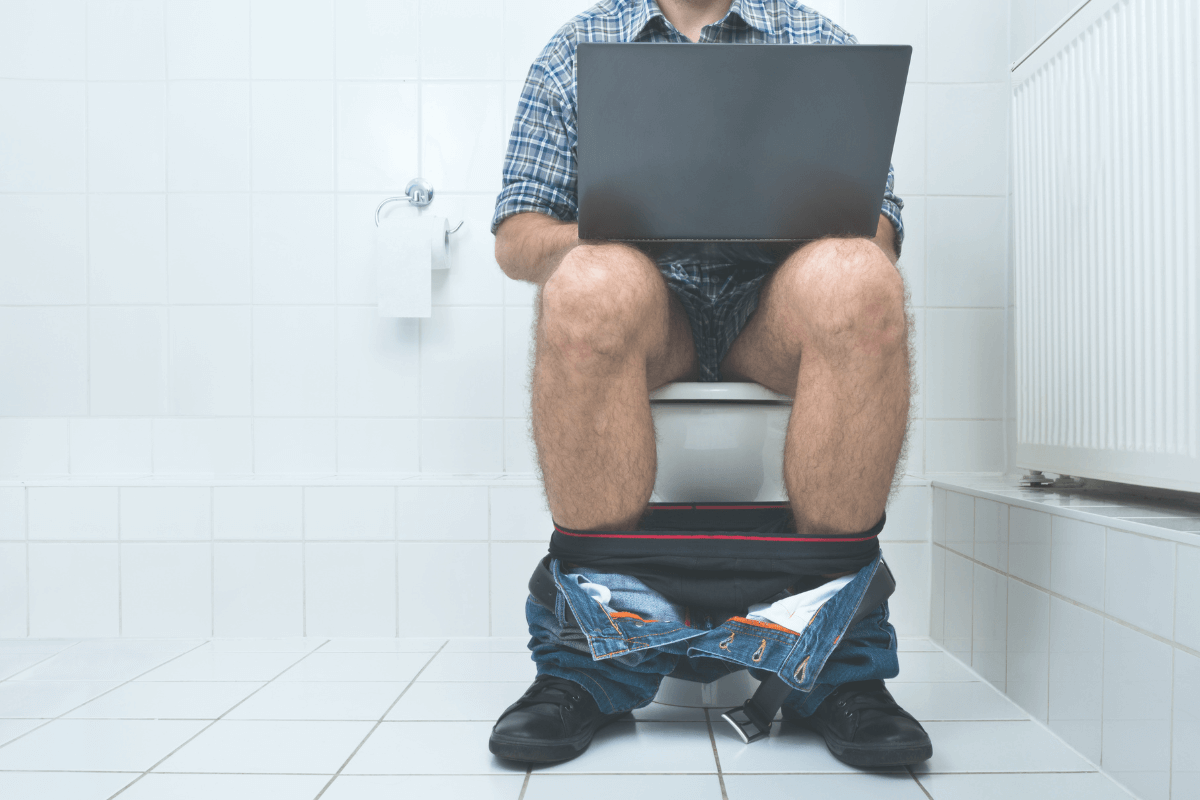 Man sitting on toilet and holding a laptop