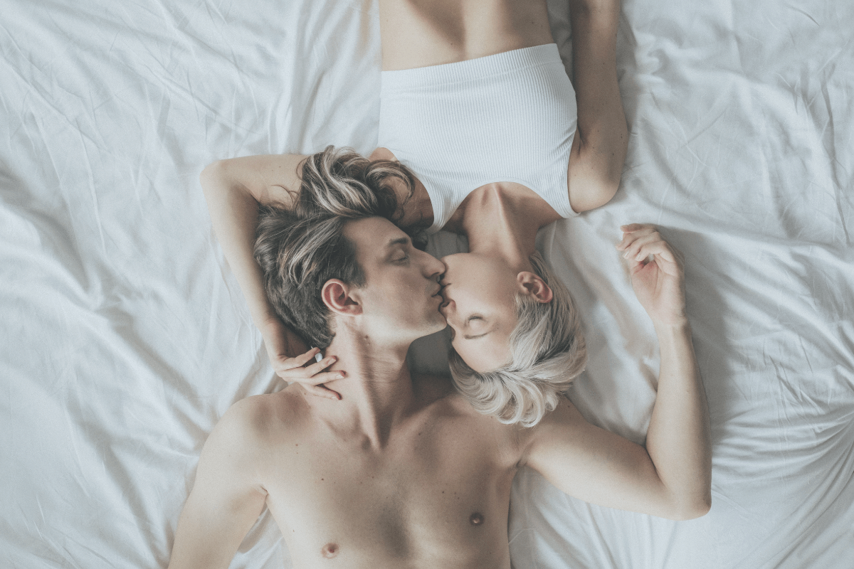 A woman and man lying in bed together and kissing each other. 