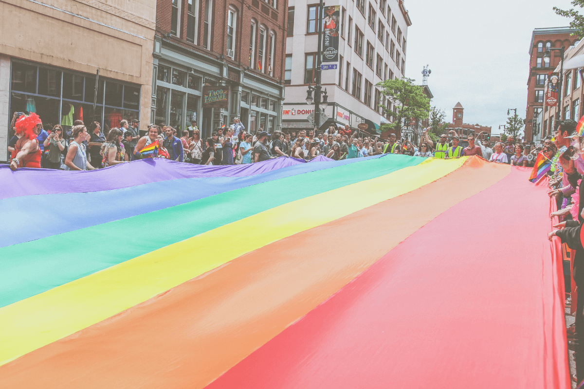 Image of a rainbow Pride flag being carried down a street during an LGBTQ+ Pride Celebration March