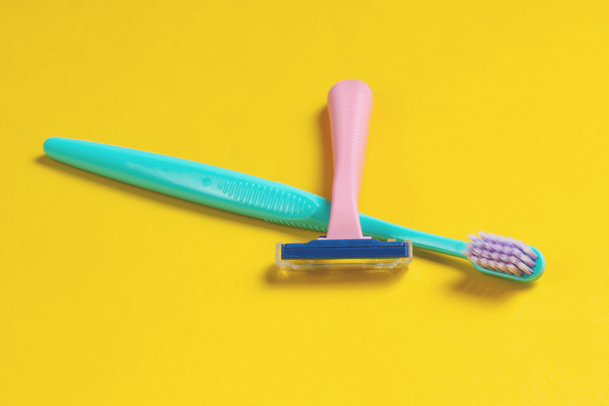 A razor and toothbrush sitting at slanted angles on a yellow background