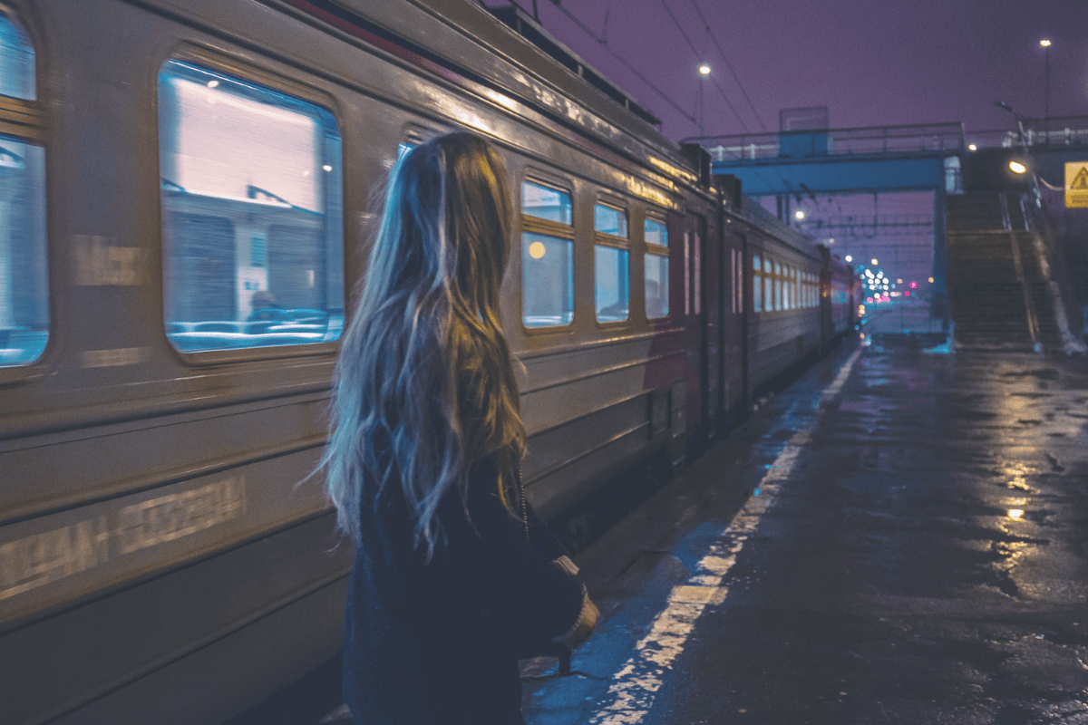 A woman steps out of a train alone and looks around. 