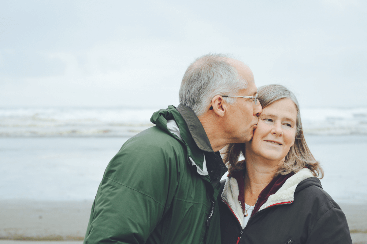 an older couple laughing together outside with a tree in the background