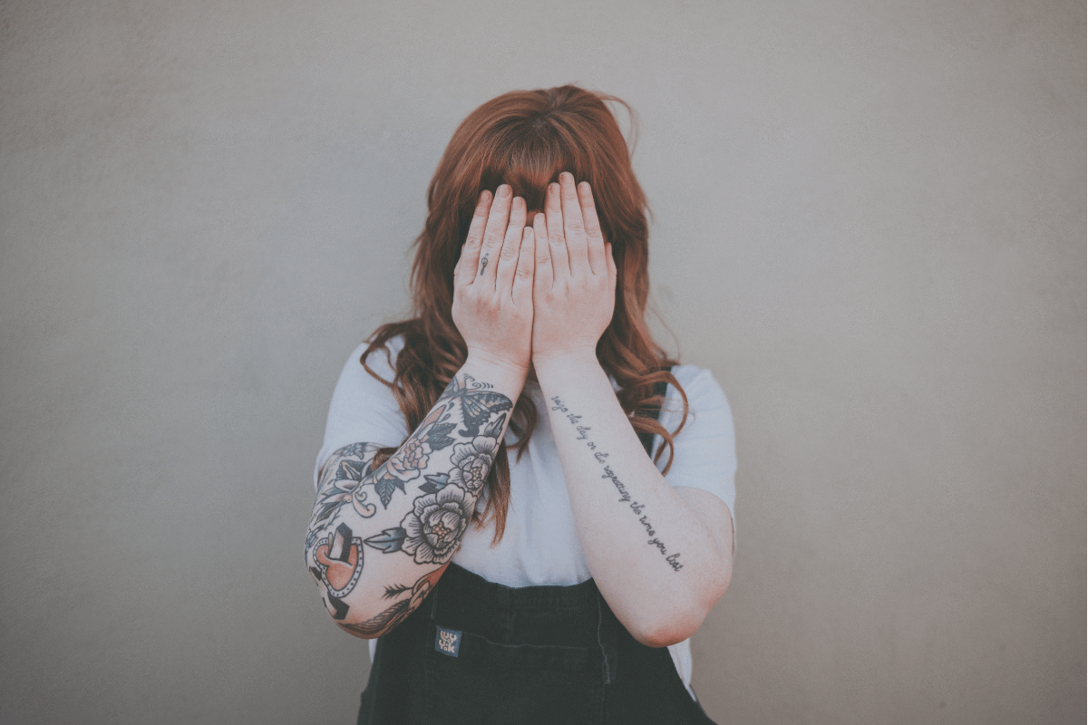 A girl with tattoos using her hands to hide her face in embarrassment