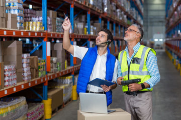 two men wearing vests working in a warehouse