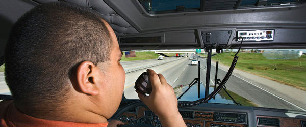 Man talking on CB radio microphone inside a tractor trailer on a highway