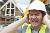 大きな騒音から耳を覆う黄色のベストを着た建設労働者の男性