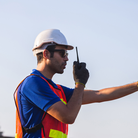 Man wearing hard hat and orange vest talking into a two-way radio