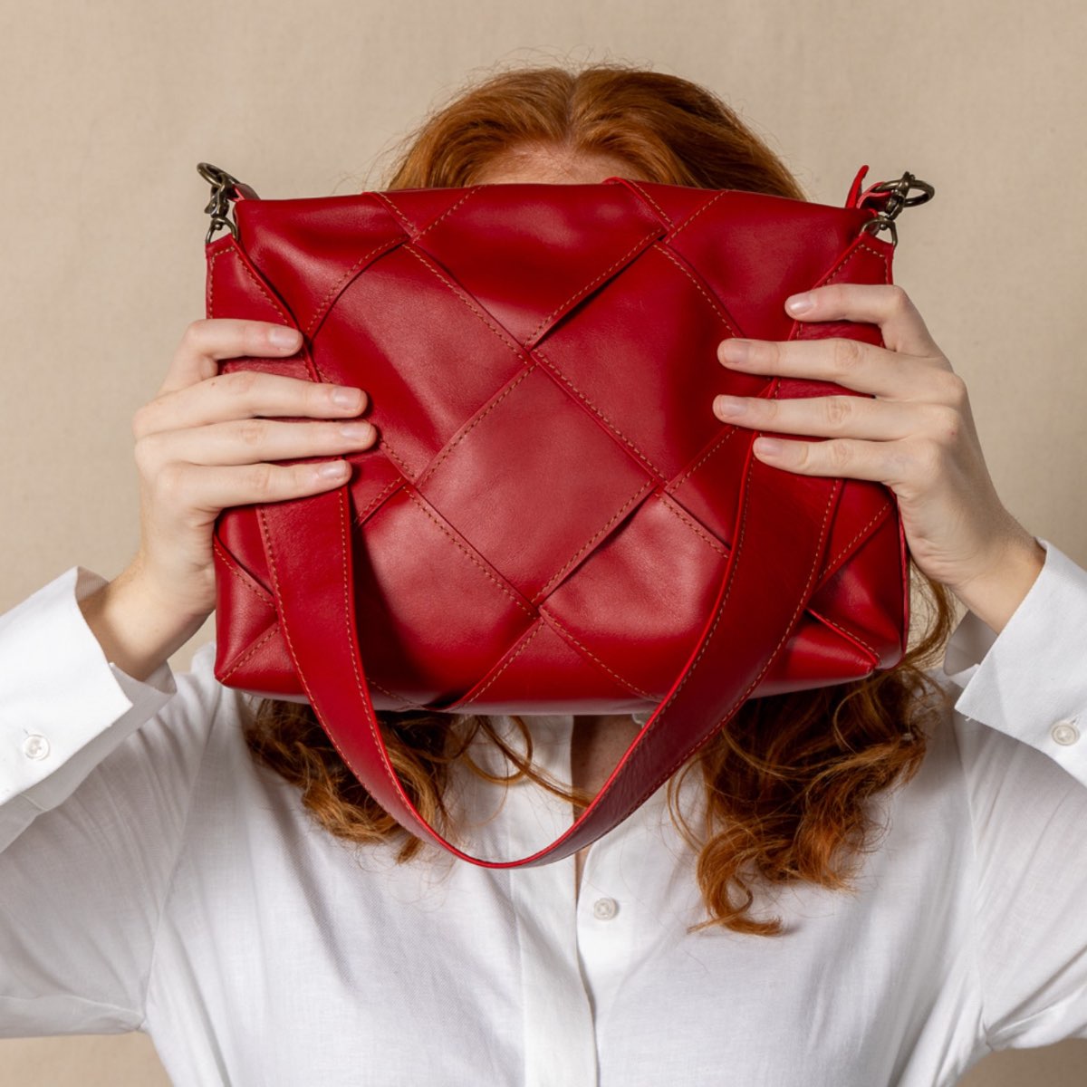 red optimal shoulder bag held in front of models face.
