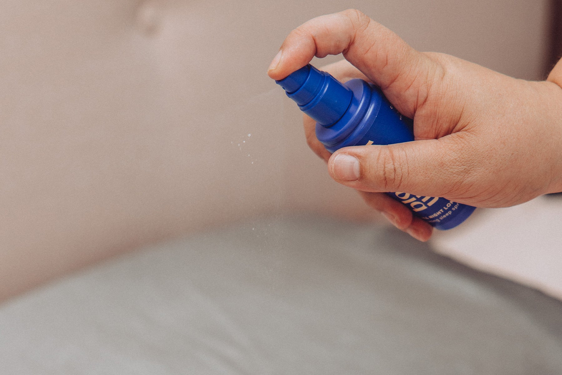 Person holding a bottle of pillow spray and spraying over the pillow