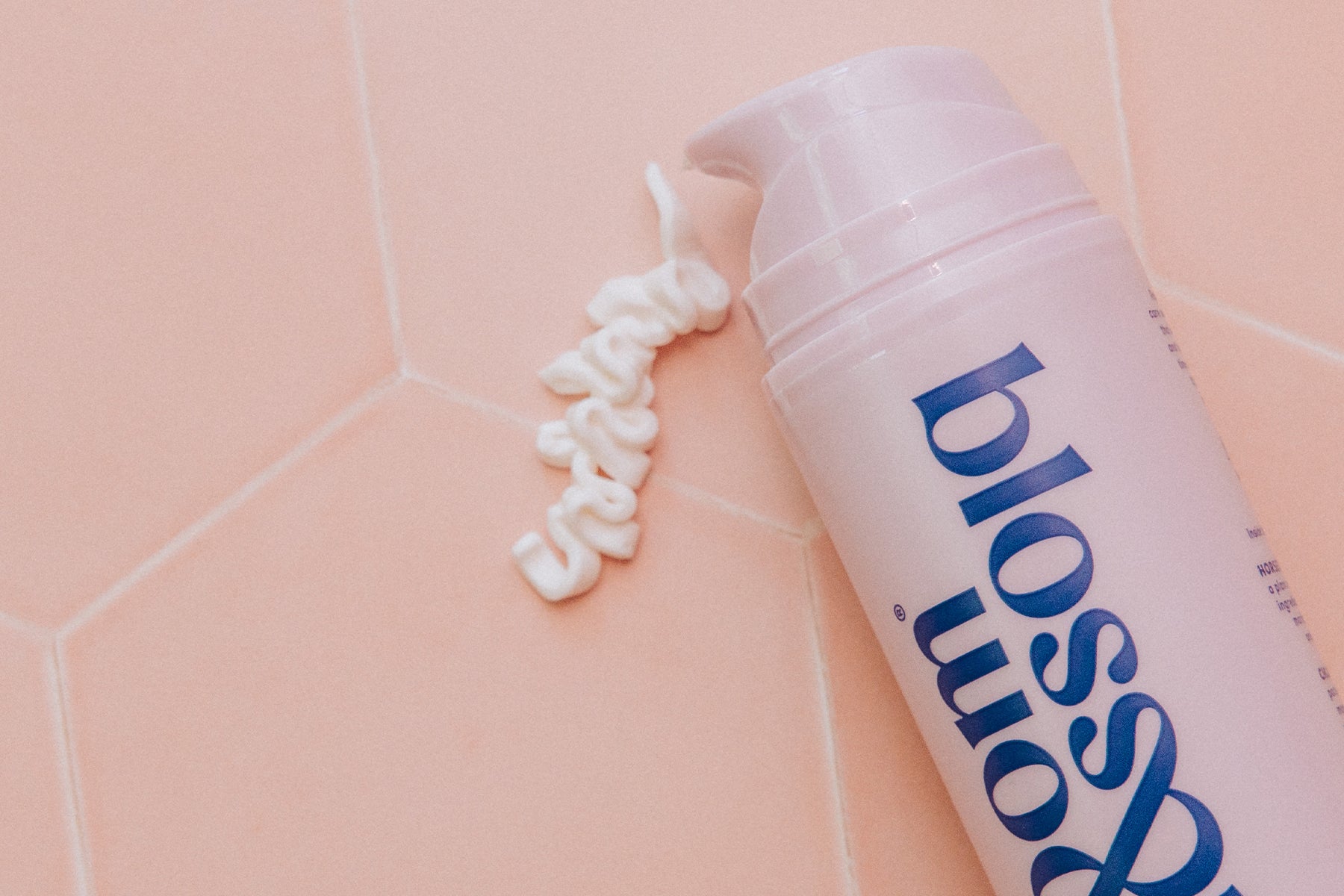 Bottle of And Stretch... Stretch mark cream being pumped out onto a tiled surface.