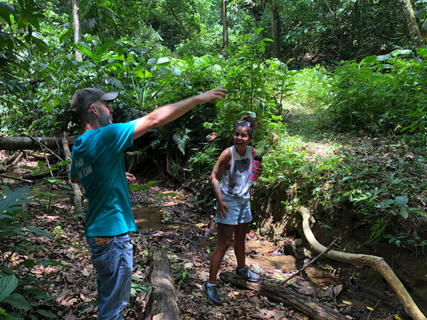 Man and woman standing in a beautiful lush Puerto Rican forest. Man is pointing at a tree and woman is laughing.