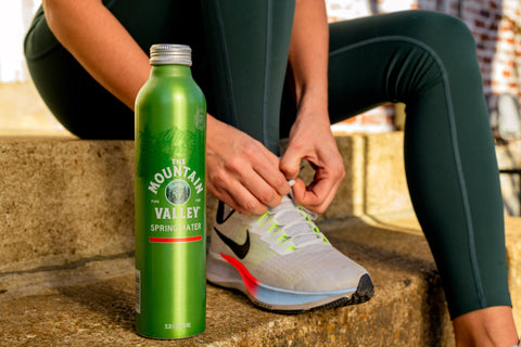 Athlete tying a tennis shoe with Mountain Valley Spring Water at her side
