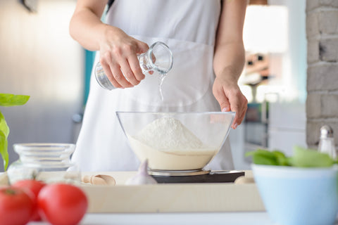 Woman pouring water into pizza dough mixture