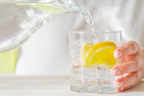 Woman pouring water over a lemon in glass