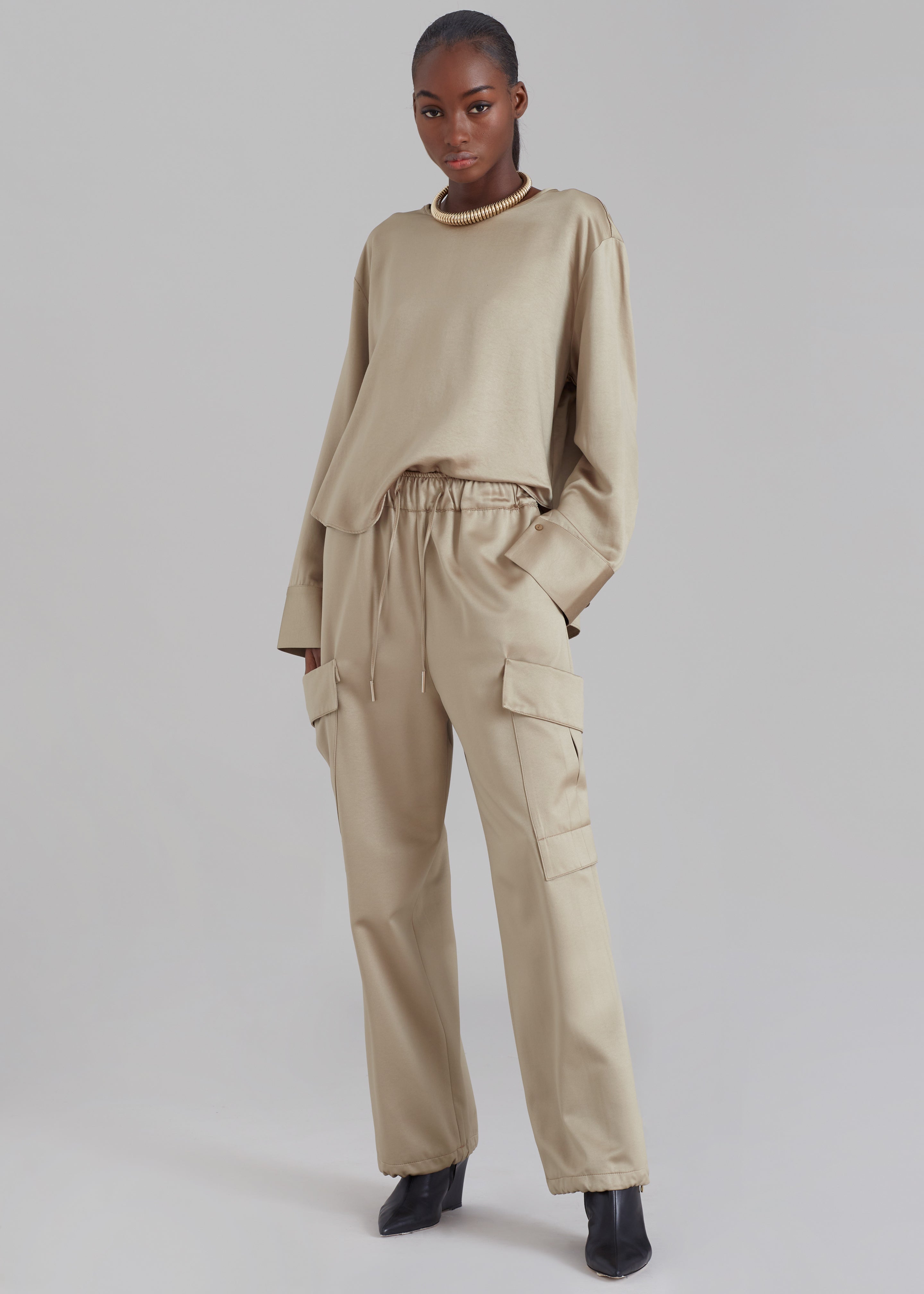 Frankie Shop Kemop silky cargo pants in bronze come in a midweight satin fabric and have an Oversized silhouette with a Straight leg and Elasticated waistband with drawstring. These cargo pants have Enlarged cargo pockets at each leg and Side seam hip pockets. The trousers have adjustable toggles at the hem