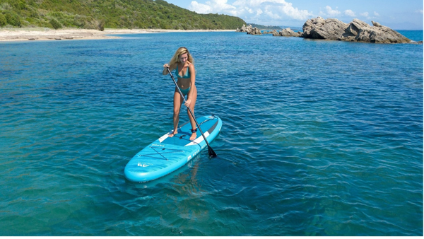 A woman rides on her blue blowup paddle board with gorgeous clear water beneath her. 