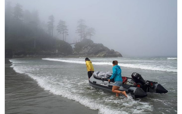 Two people drag their inflatable boat up to shore. 