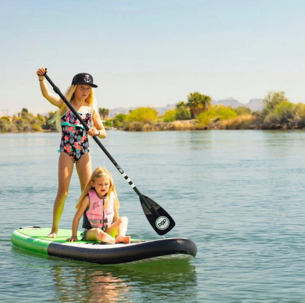 Two little sisters with blonde hair paddle board together. 